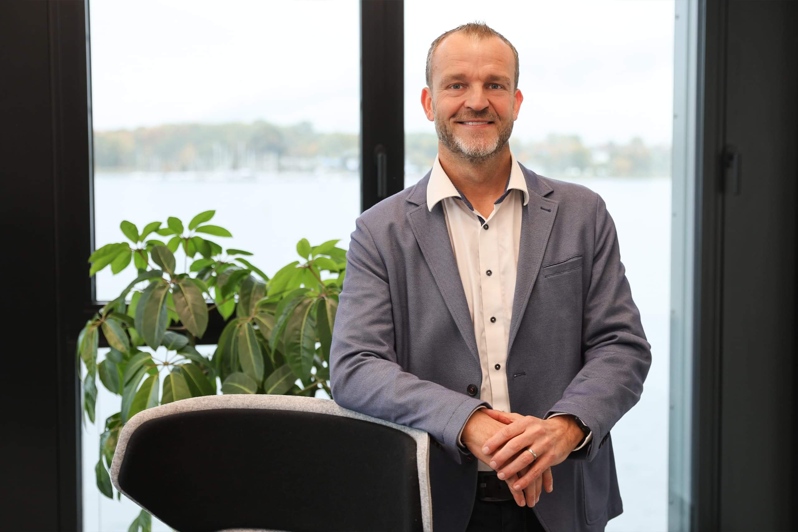 Gösta Falkenberg Gösta Falkenberg steht an einen Stuhl lehnend in seinem Büro vor großen Fenstern.