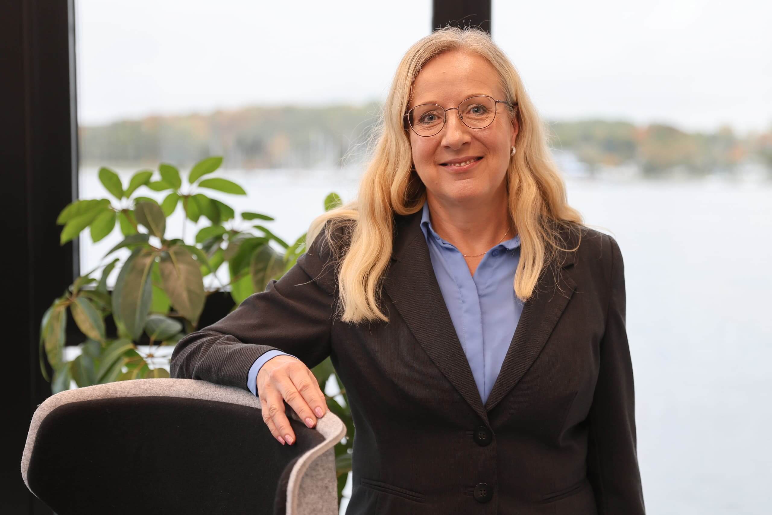 Veronika Westphal Veronika Westphal steht an einen Stuhl lehnend in ihrem Büro vor großen Fenstern.
